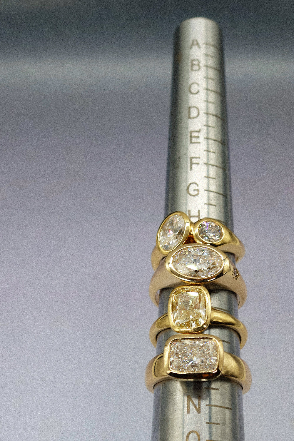 four gold rings of various designs and shapes all set with diamonds on a ring sizer tool