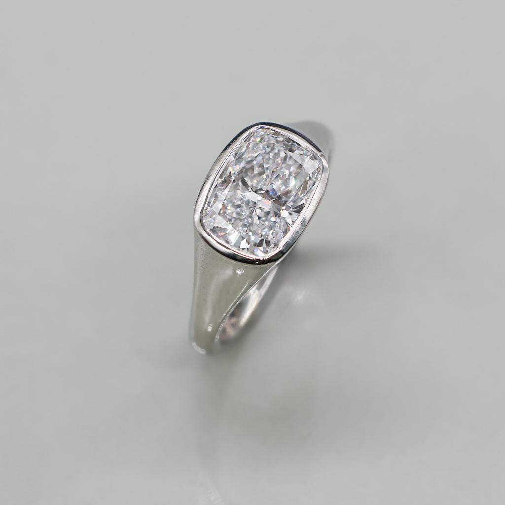 A cushion-cut diamond ring in a white gold setting, photographed on a clean, light reflective surface.