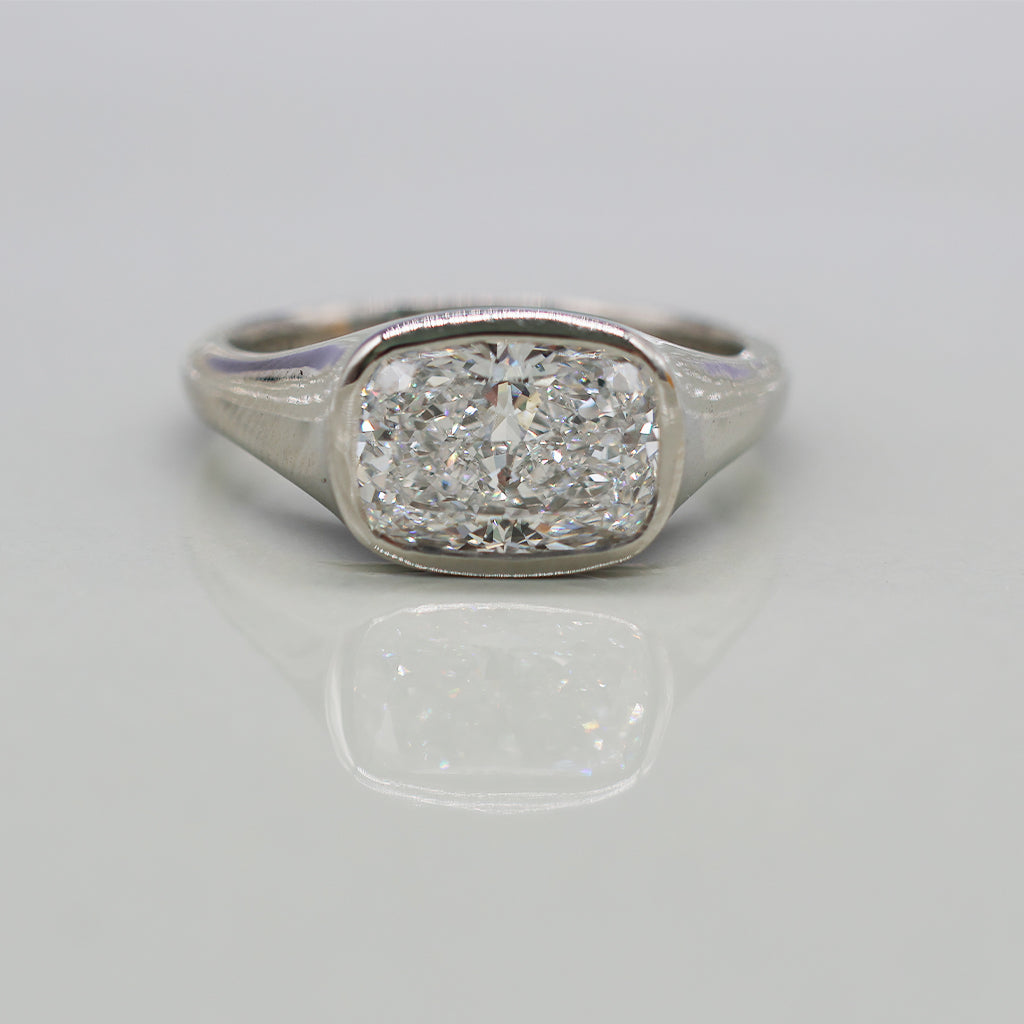 A cushion-cut diamond ring in a white gold setting, photographed on a clean, light reflective surface.