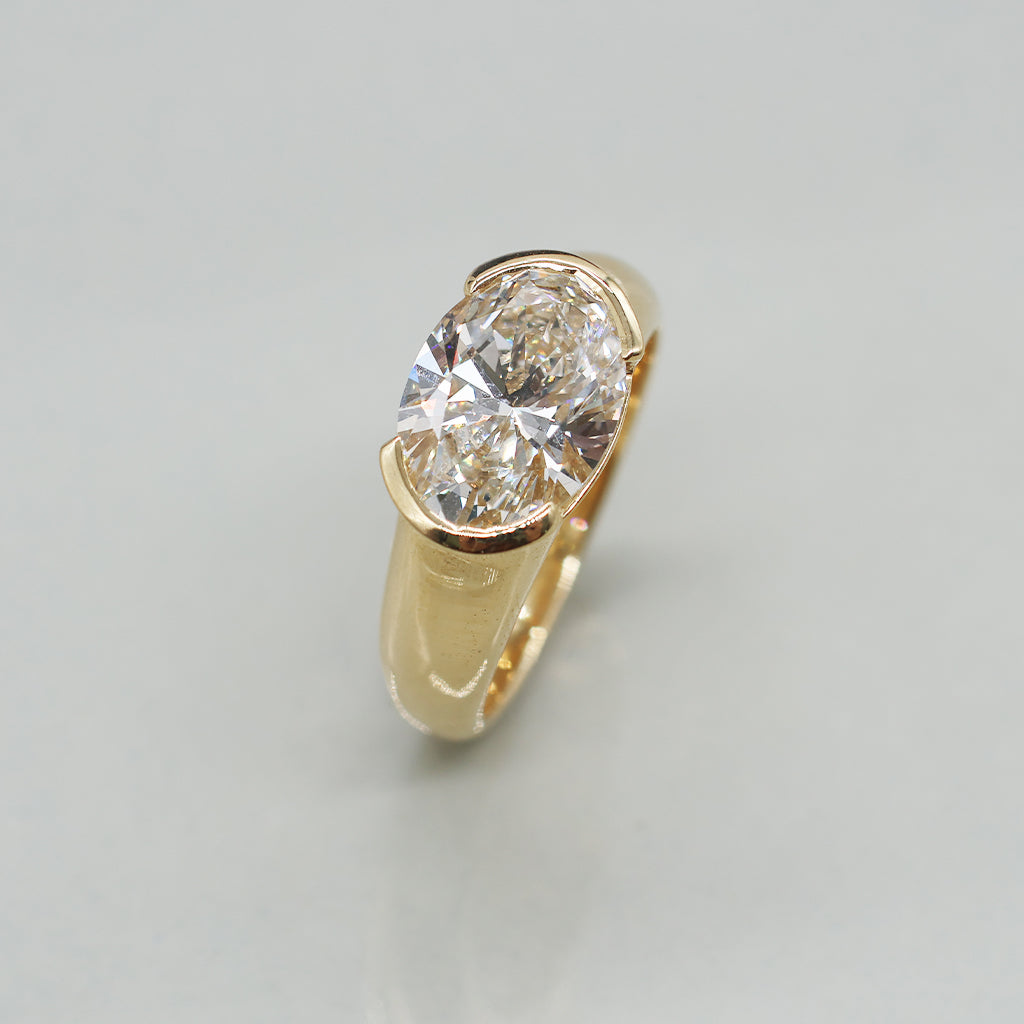 An oval-cut diamond ring set in a yellow gold band, photographed on a clean, light background.