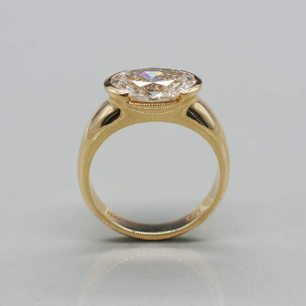 An oval-cut diamond ring set in a yellow gold band, photographed on a clean, light background.