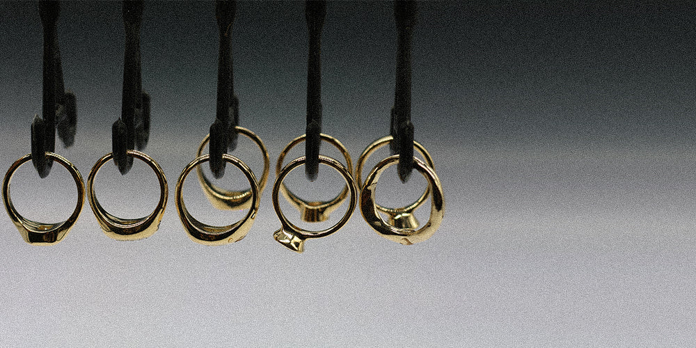 Five gold rings hanging from black display hooks against a dark-to-light gray gradient background.
