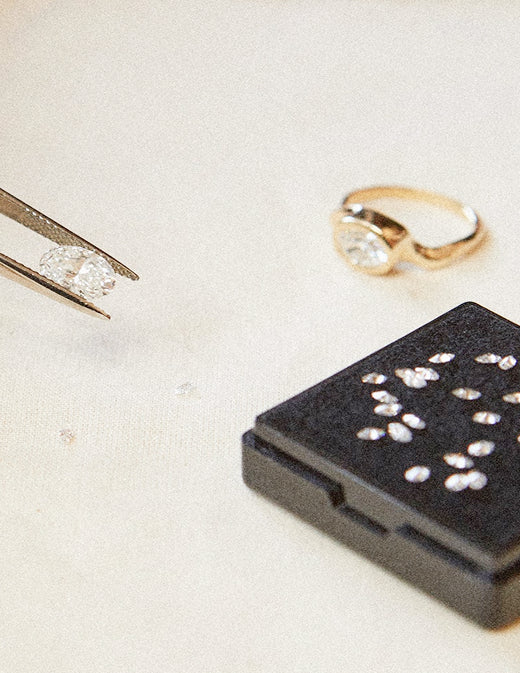 Gold diamond ring set beside a collection of small loose diamonds and tweezers holding a loose oval diamond over the top