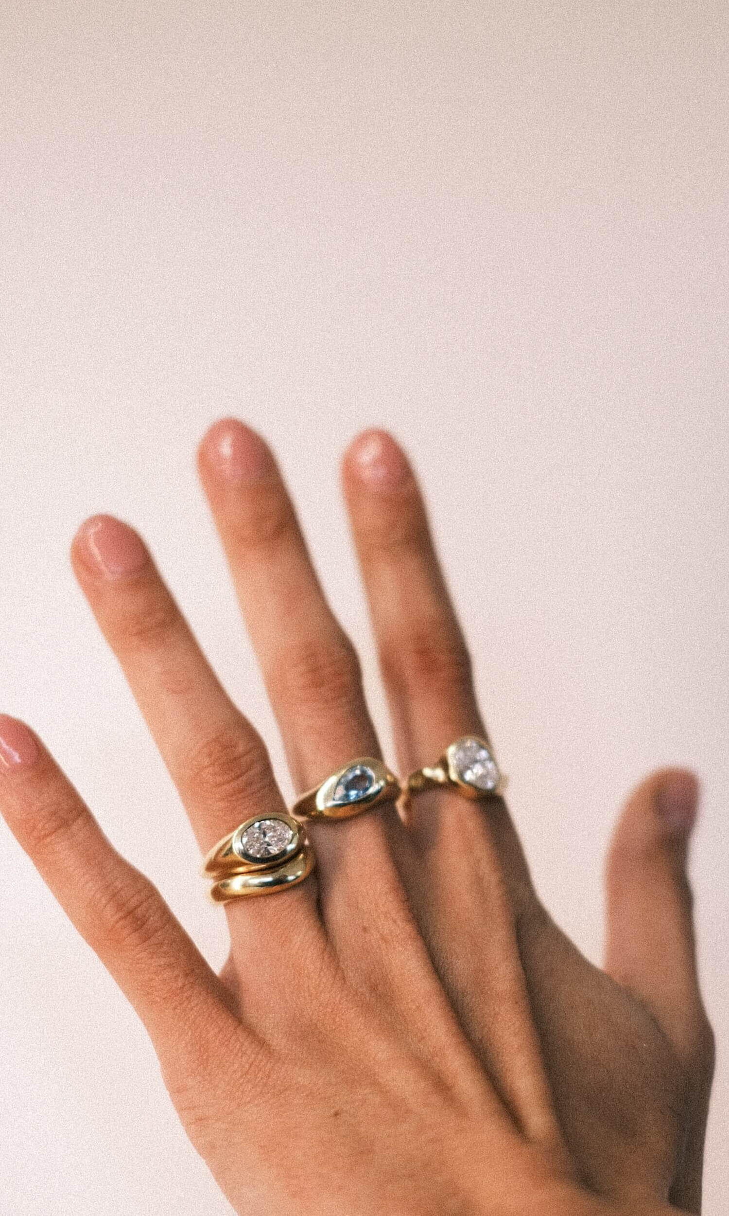 Tall image of a hand wearing 4 gold rings of alternate styles