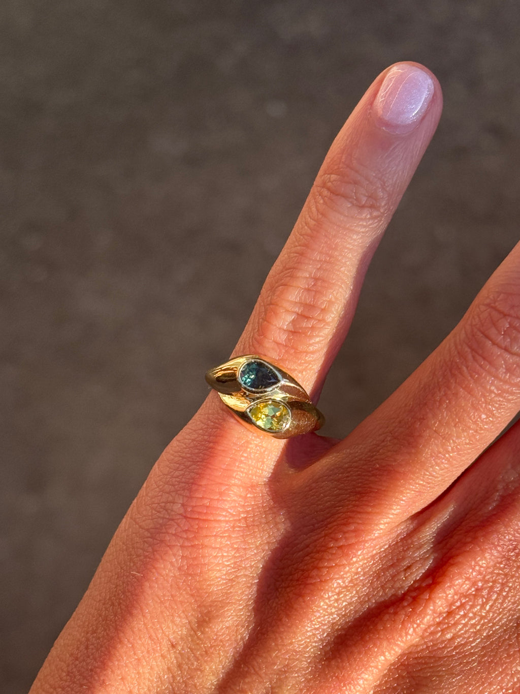 Gold ring with gemstones on a finger against a neutral background