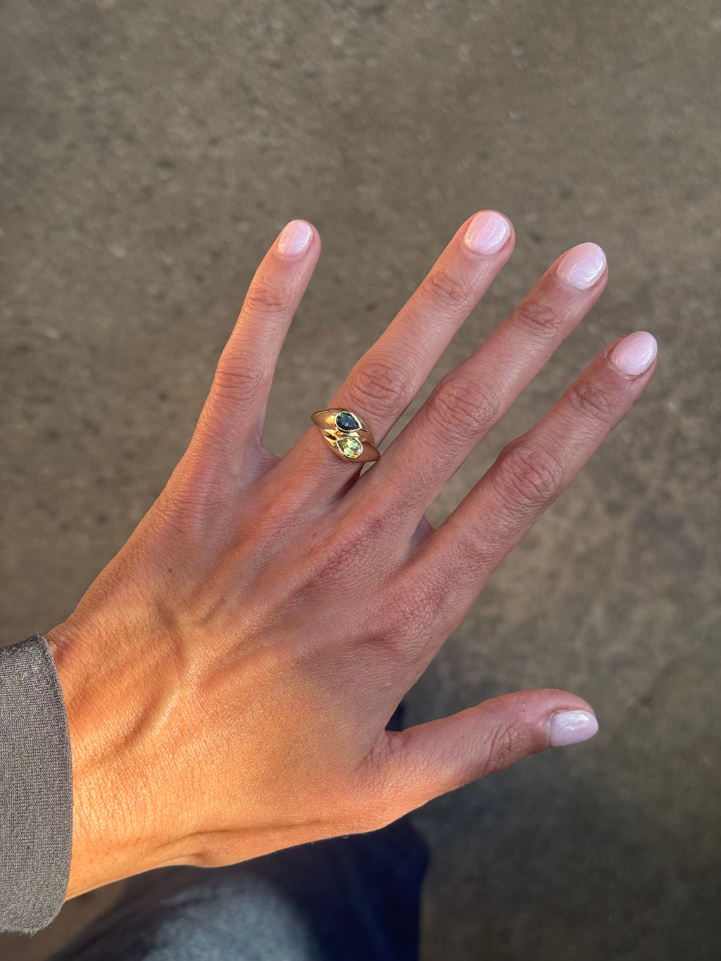Hand wearing a ring with a green gemstone on a neutral background