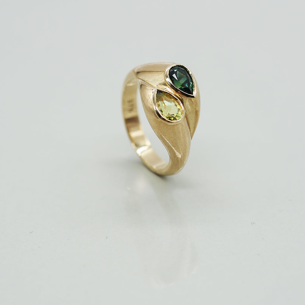 Gold ring with green gemstones on a light gray background