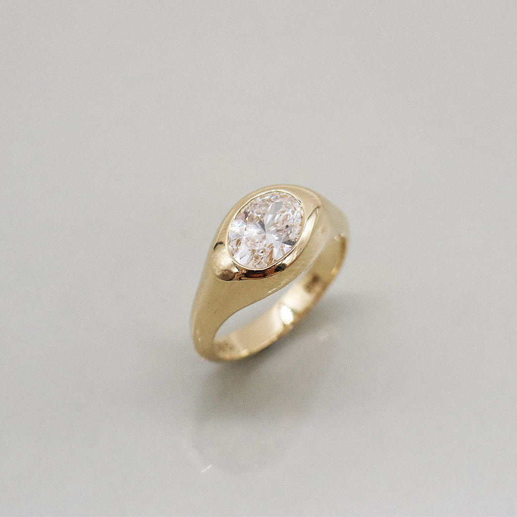 A yellow gold oval ring featuring a large oval brilliant-cut diamond center stone set against a clean white background with a soft reflection.