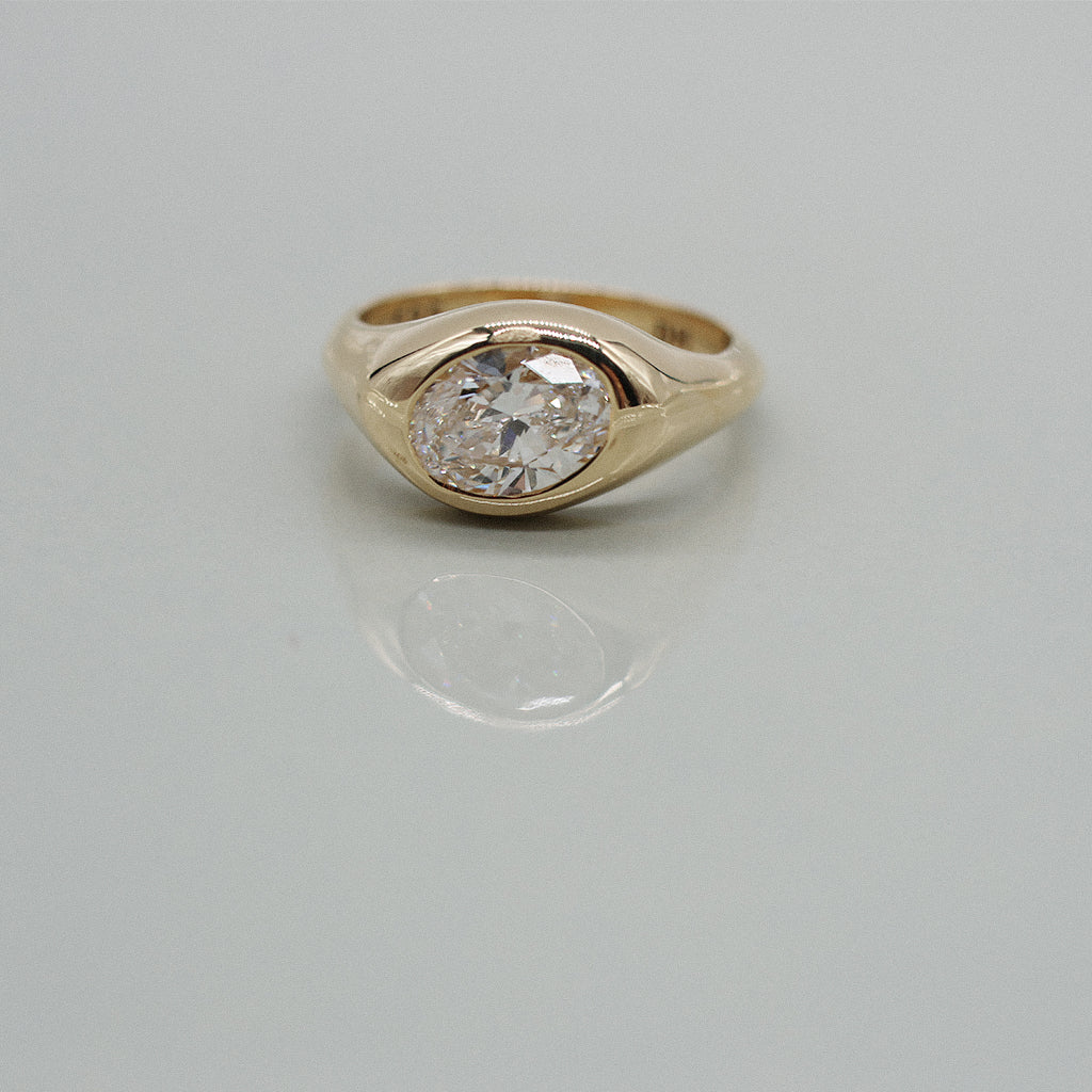 A yellow gold oval ring featuring a large oval brilliant-cut diamond centre stone set against a clean white background with a soft reflection.