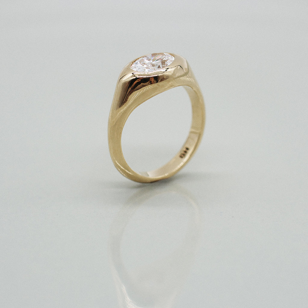 A yellow gold oval ring featuring a large oval brilliant-cut diamond center stone set against a clean white background with a soft reflection.