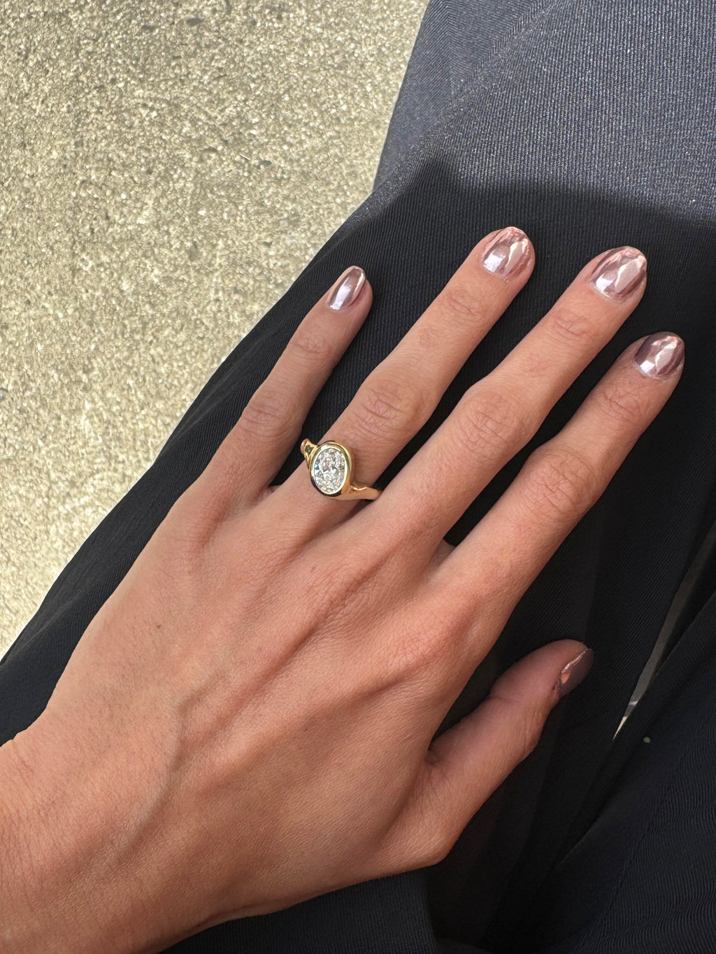 A gold ring with a central diamond stone, showcasing an asymmetrical and subtly textured band, displayed on a person's finger.