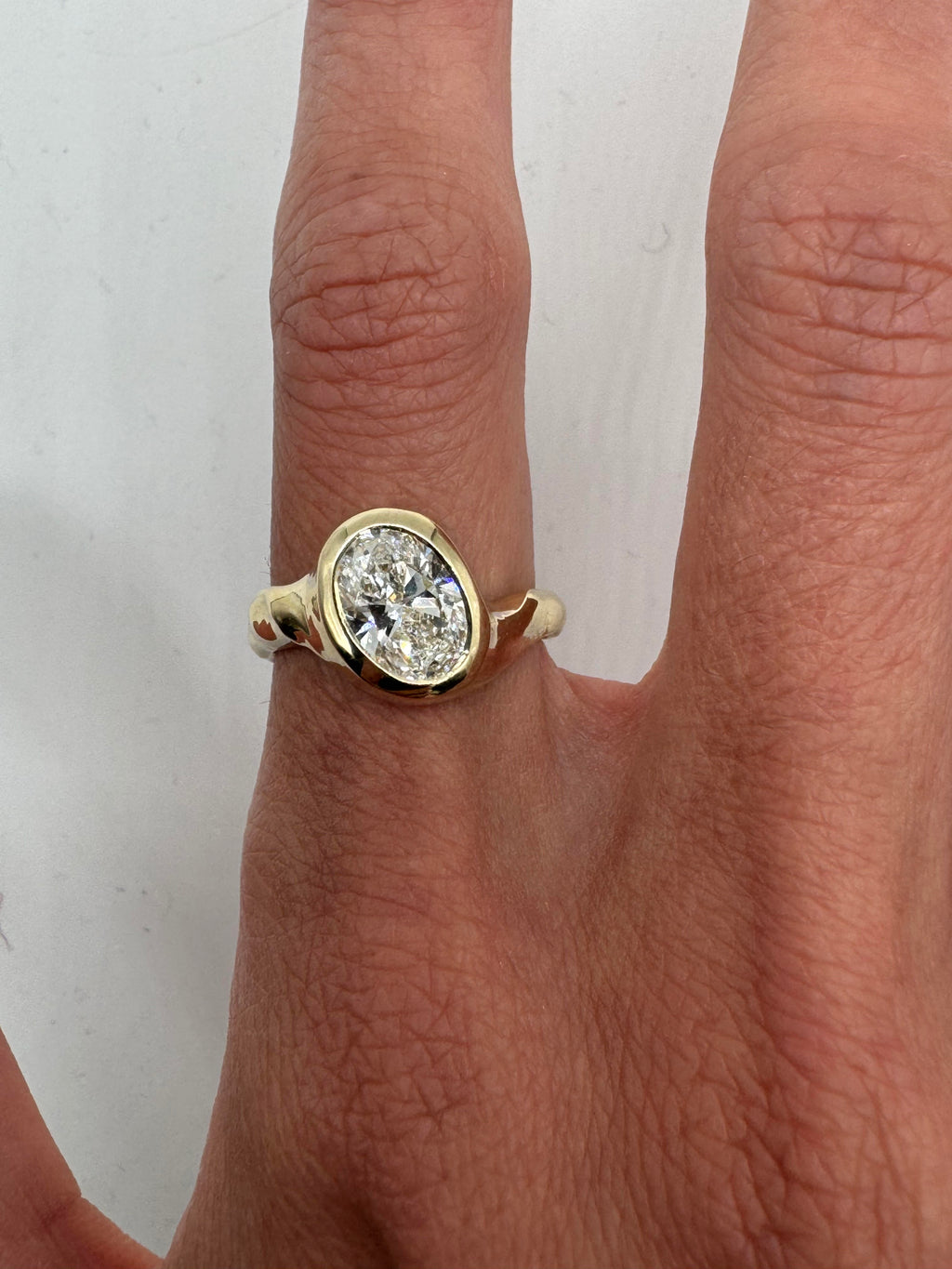 A gold ring with a central diamond stone, showcasing an asymmetrical and subtly textured band, displayed on a person's finger.