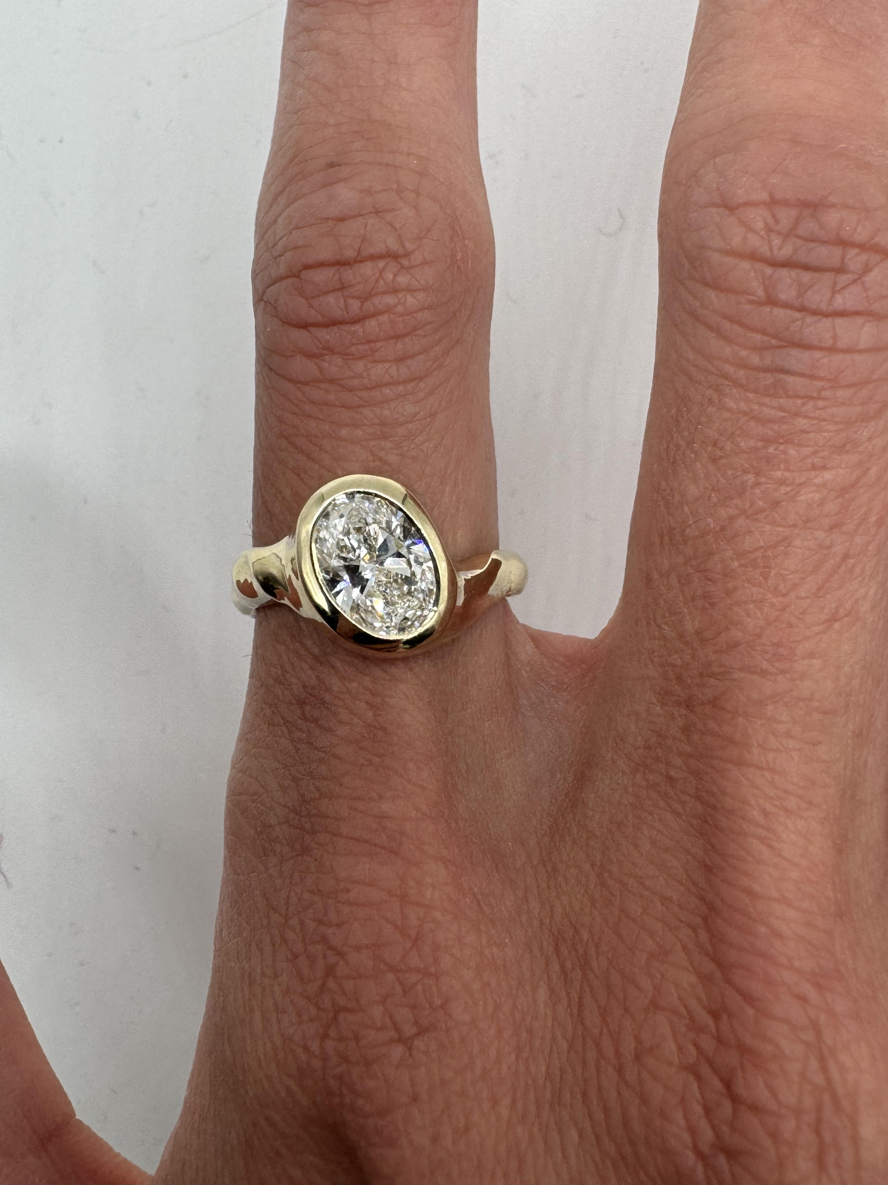 A gold ring with a central diamond stone, showcasing an asymmetrical and subtly textured band, displayed on a person's finger.