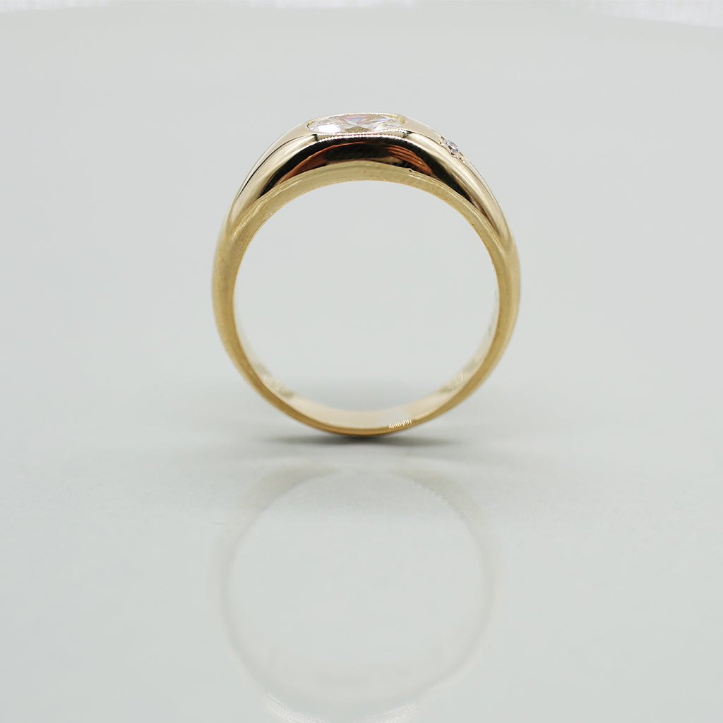 A yellow gold oval ring featuring a large oval brilliant-cut diamond center stone and a small round diamond accent on the band, set against a clean white background with a soft reflection.