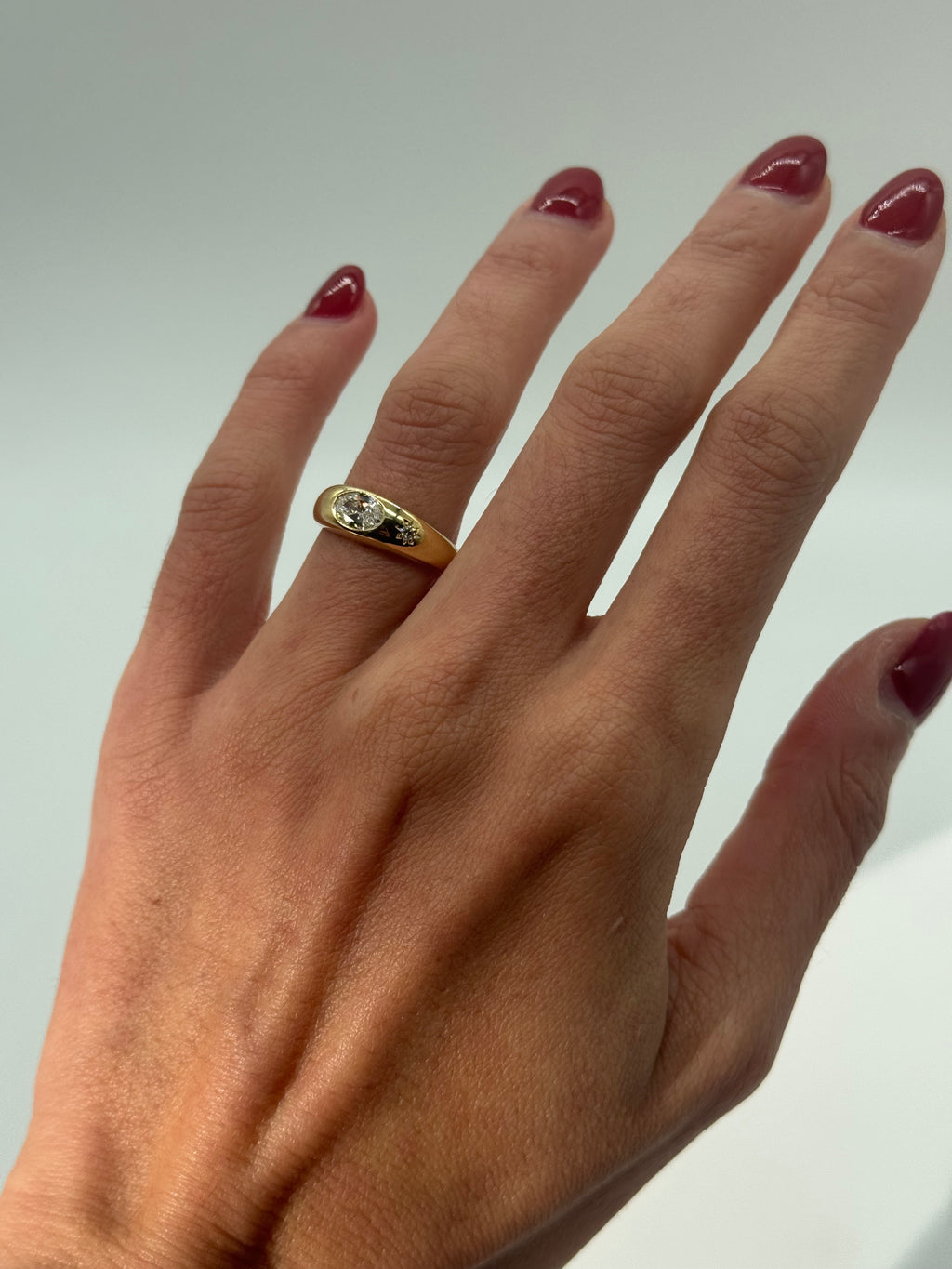 Hand wearing a gold ring with a diamond on a plain background