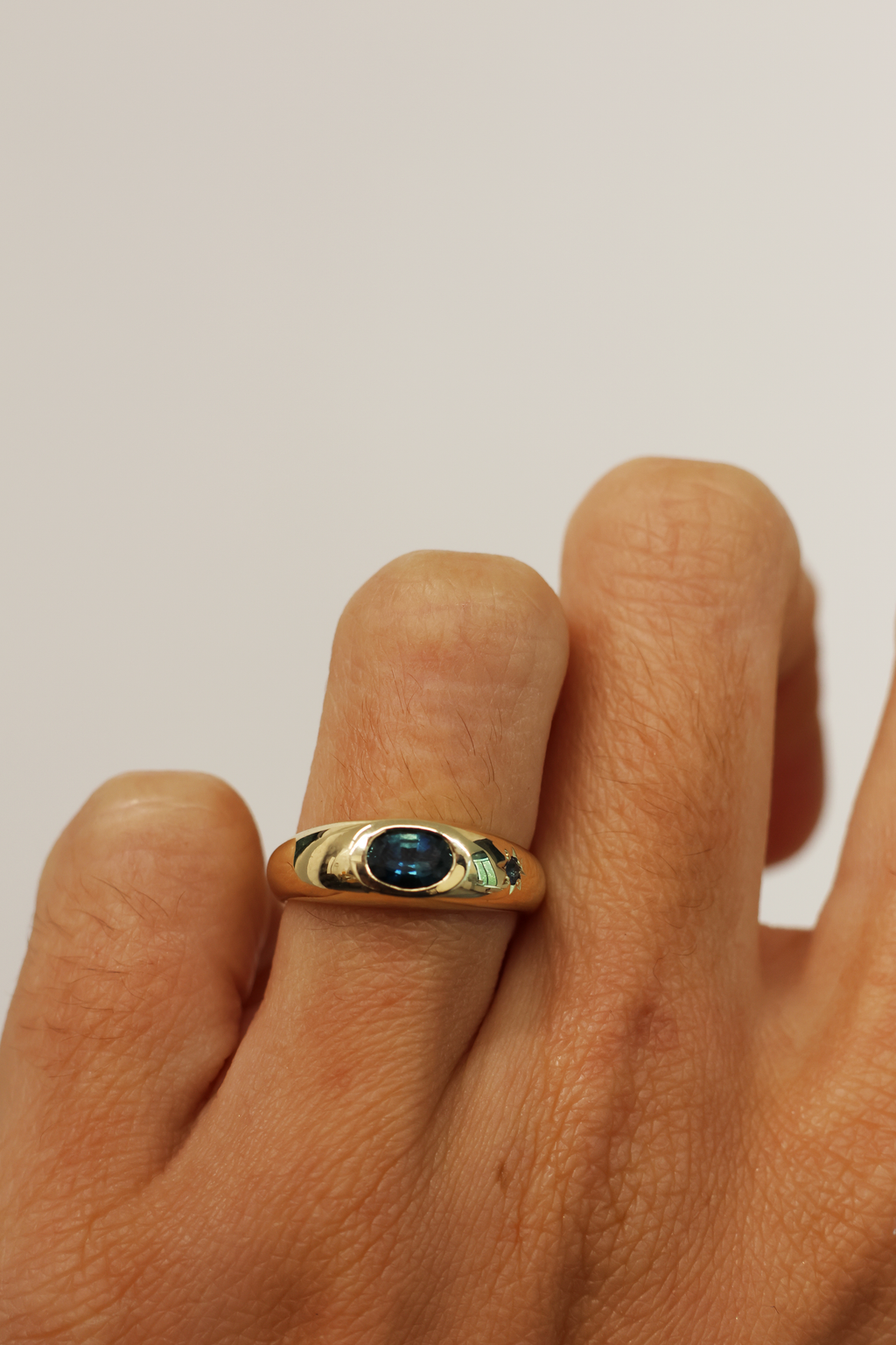 Gold ring with a blue gemstone on a finger against a plain background