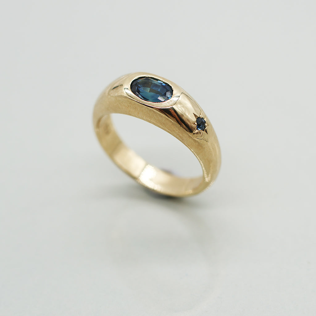 Gold ring with a blue gemstone on a light gray background