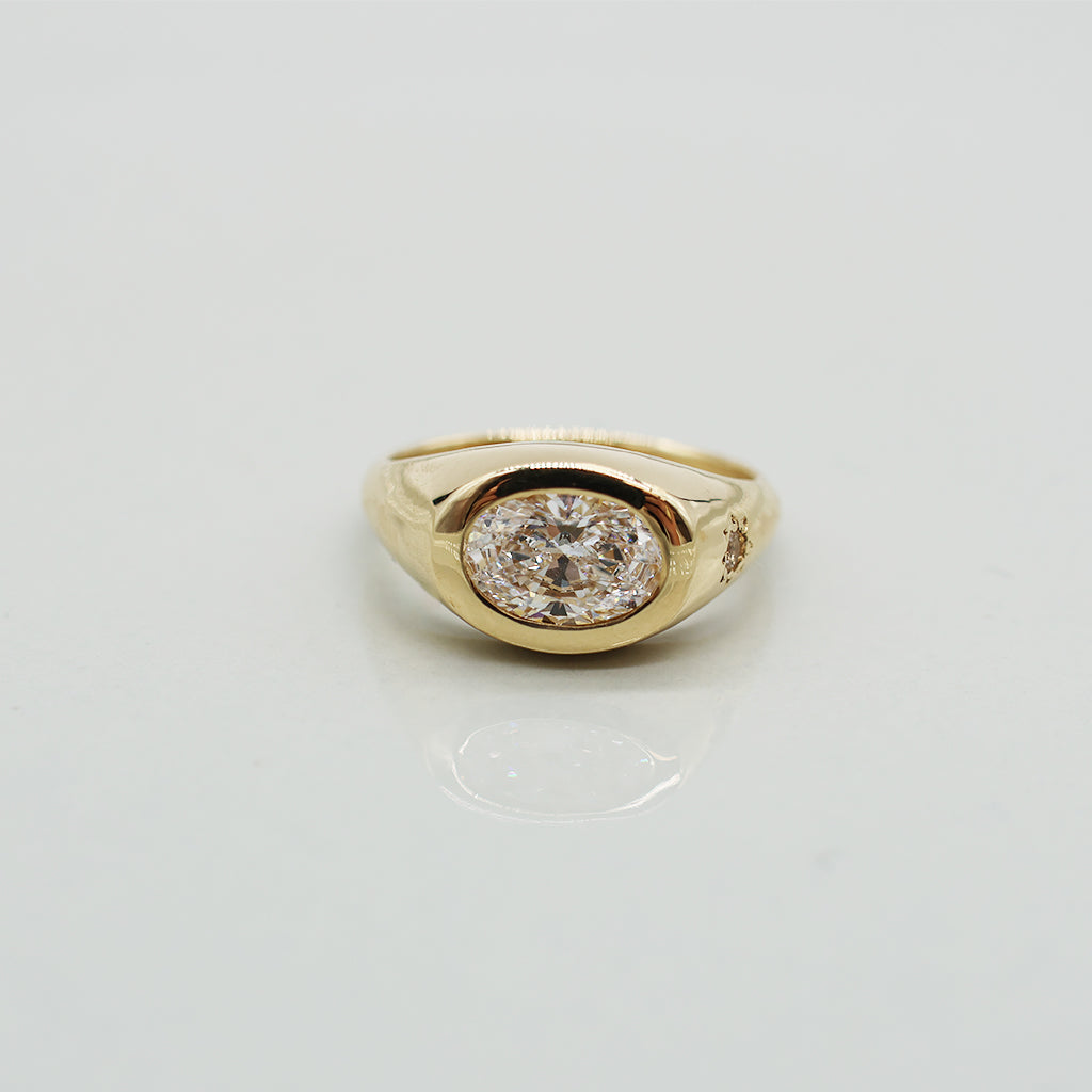 A yellow gold oval ring featuring a large oval brilliant-cut diamond centre stone set against a clean white background with a soft reflection.