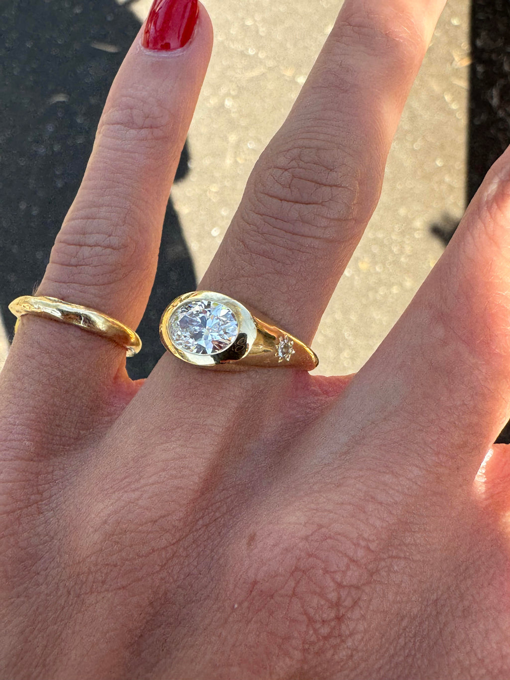 A yellow gold oval ring featuring a large oval brilliant-cut diamond centre stone set featured on the hand with grey sunlit background.