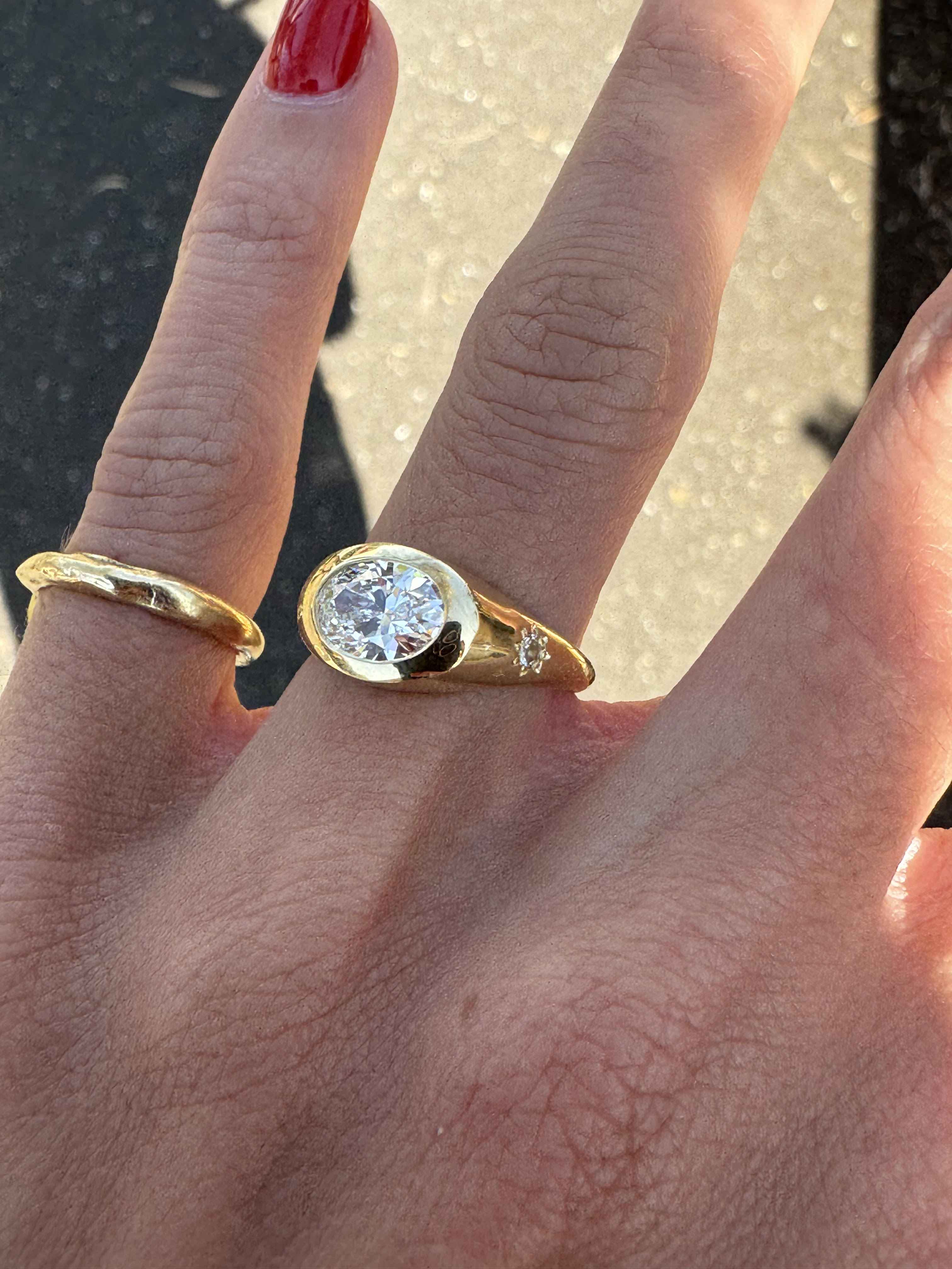 A yellow gold oval ring featuring a large oval brilliant-cut diamond centre stone set featured on the hand with grey sunlit background.