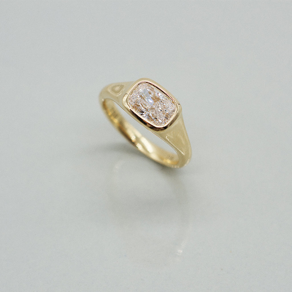 A yellow gold cushion ring featuring a large cushion brilliant-cut diamond center stone, set against a clean white background with a soft reflection.