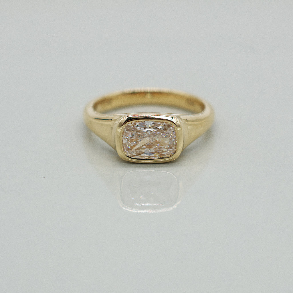 A yellow gold cushion ring featuring a large cushion brilliant-cut diamond center stone, set against a clean white background with a soft reflection.