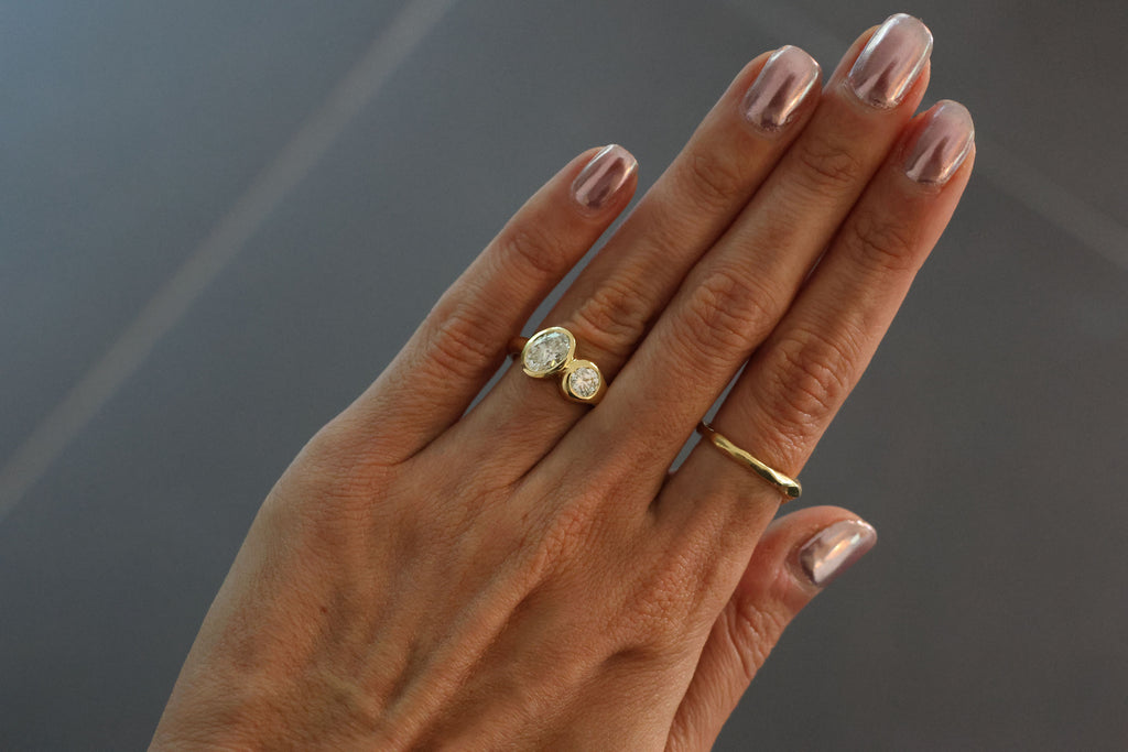 A yellow gold ring featuring a large oval brilliant-cut diamond and round diamond, on the hand, dark grey background