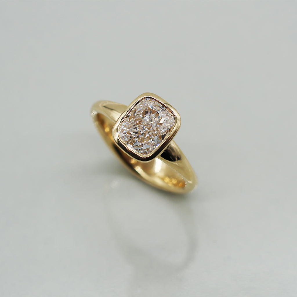 A yellow gold cushion ring featuring a large cushion brilliant-cut diamond center stone, set against a clean white background with a soft reflection.