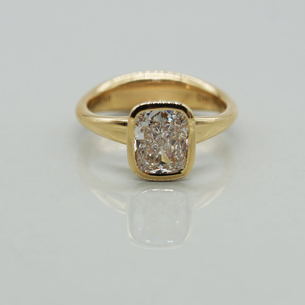A yellow gold cushion ring featuring a large cushion brilliant-cut diamond center stone, set against a clean white background with a soft reflection.
