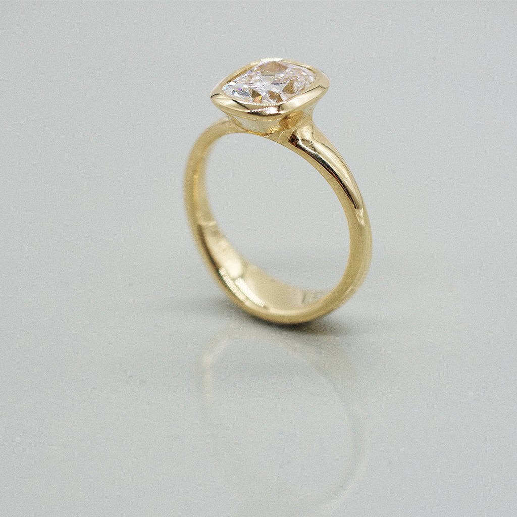 A yellow gold cushion ring featuring a large cushion brilliant-cut diamond center stone, set against a clean white background with a soft reflection.