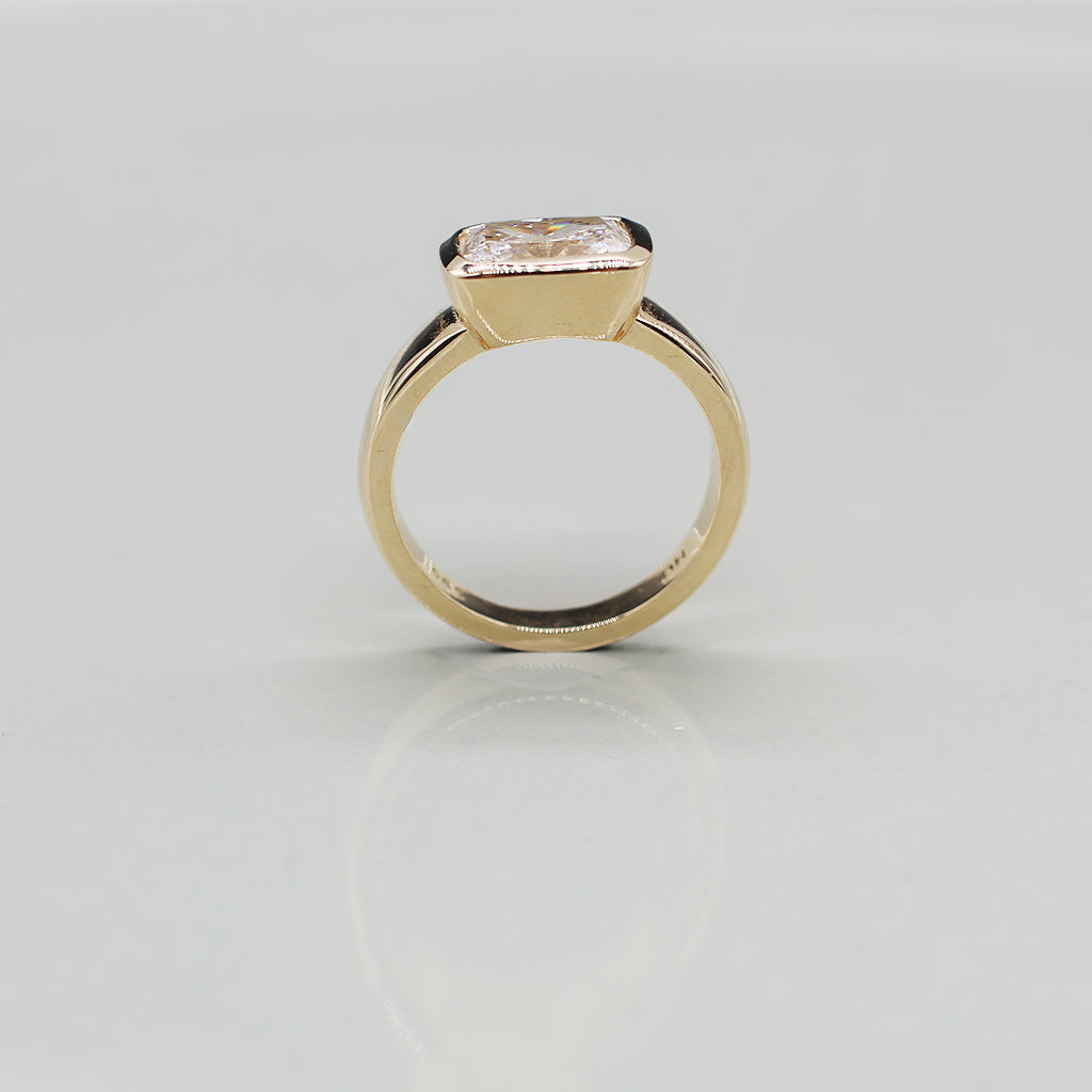 A yellow gold oval ring featuring a large cushion brilliant-cut diamond centre stone set against a clean white background with a soft reflection.