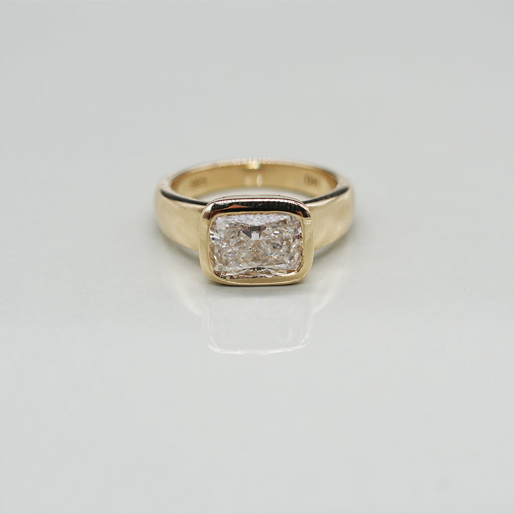 A yellow gold oval ring featuring a large cushion brilliant-cut diamond centre stone set against a clean white background with a soft reflection.
