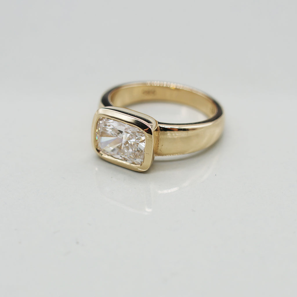 A yellow gold oval ring featuring a large cushion brilliant-cut diamond centre stone set against a clean white background with a soft reflection.