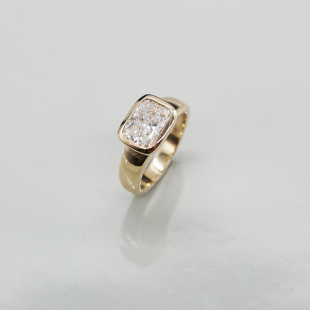 A yellow gold oval ring featuring a large cushion brilliant-cut diamond centre stone set against a clean white background with a soft reflection.