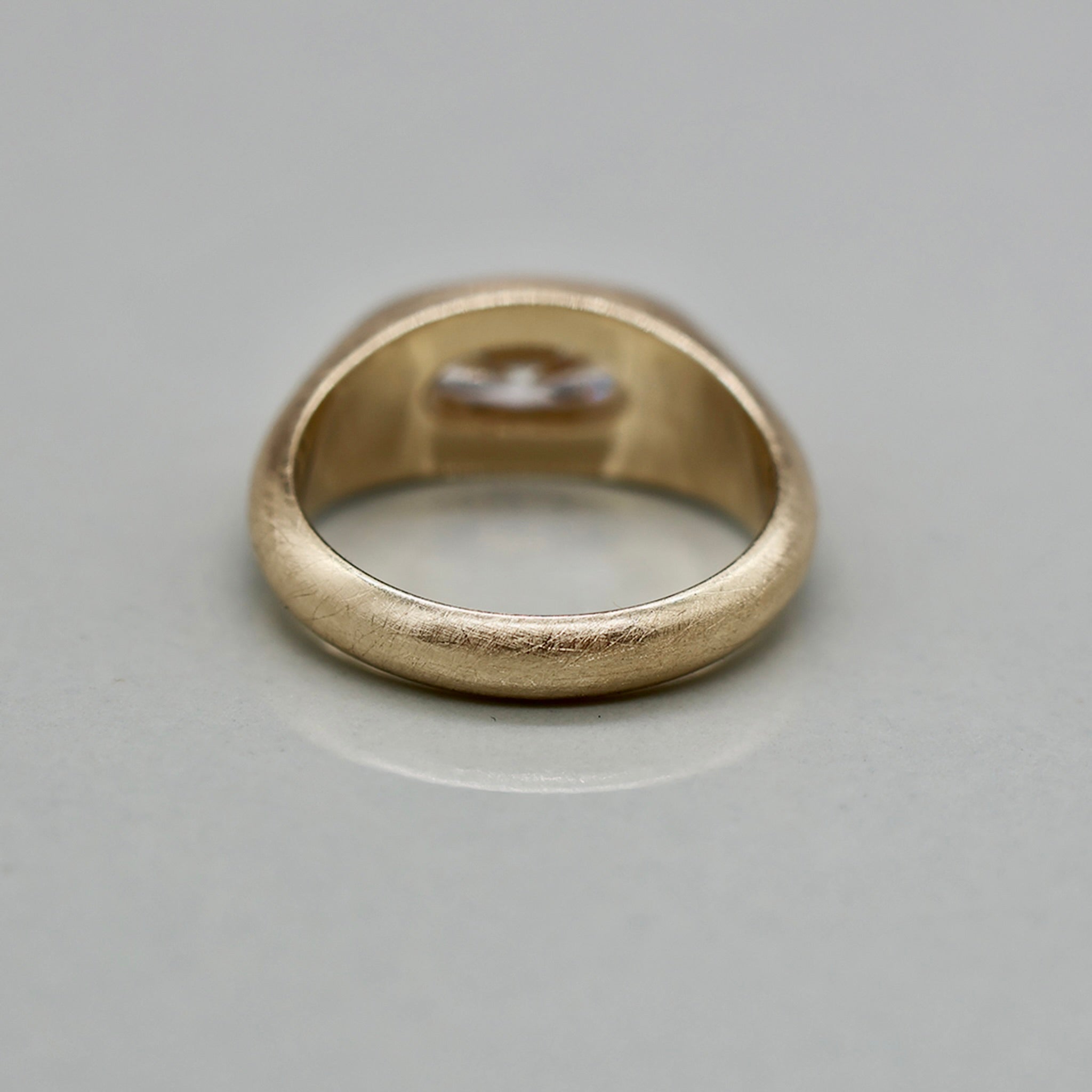 A yellow gold ring featuring a large oval brilliant-cut diamond centre stone with brushed texture, set against a clean white background with a soft reflection.