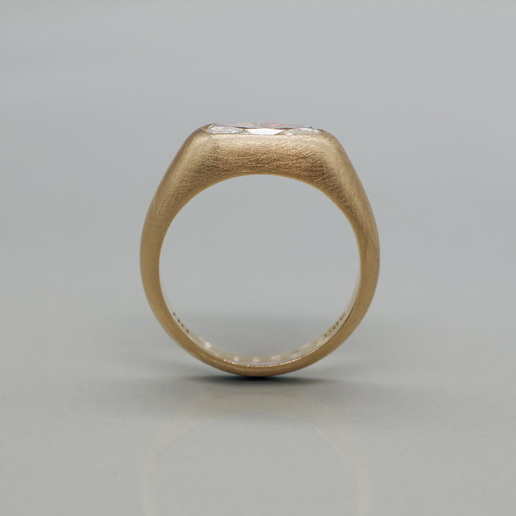 A yellow gold ring featuring a large oval brilliant-cut diamond centre stone with brushed texture, set against a clean white background with a soft reflection.