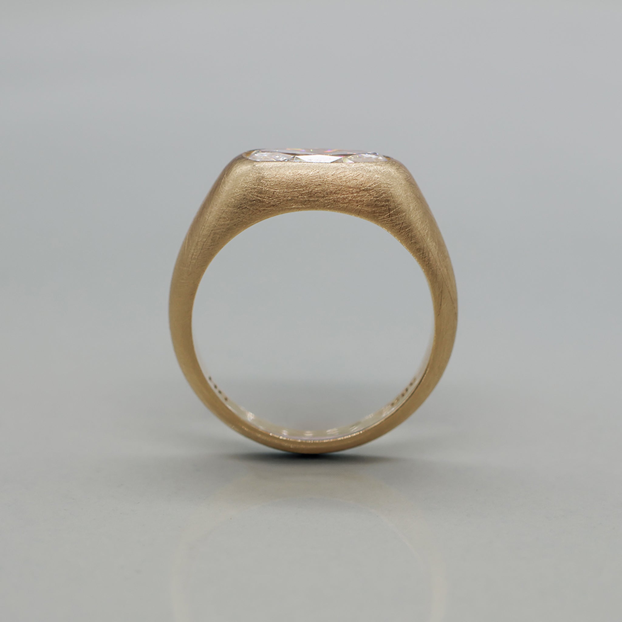 A yellow gold ring featuring a large oval brilliant-cut diamond centre stone with brushed texture, set against a clean white background with a soft reflection.
