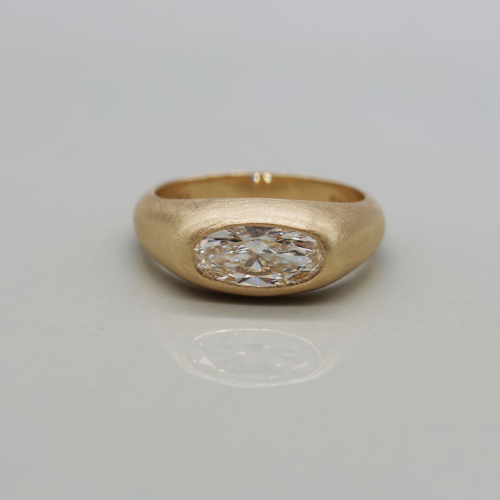 A yellow gold ring featuring a large oval brilliant-cut diamond centre stone with brushed texture, set against a clean white background with a soft reflection.