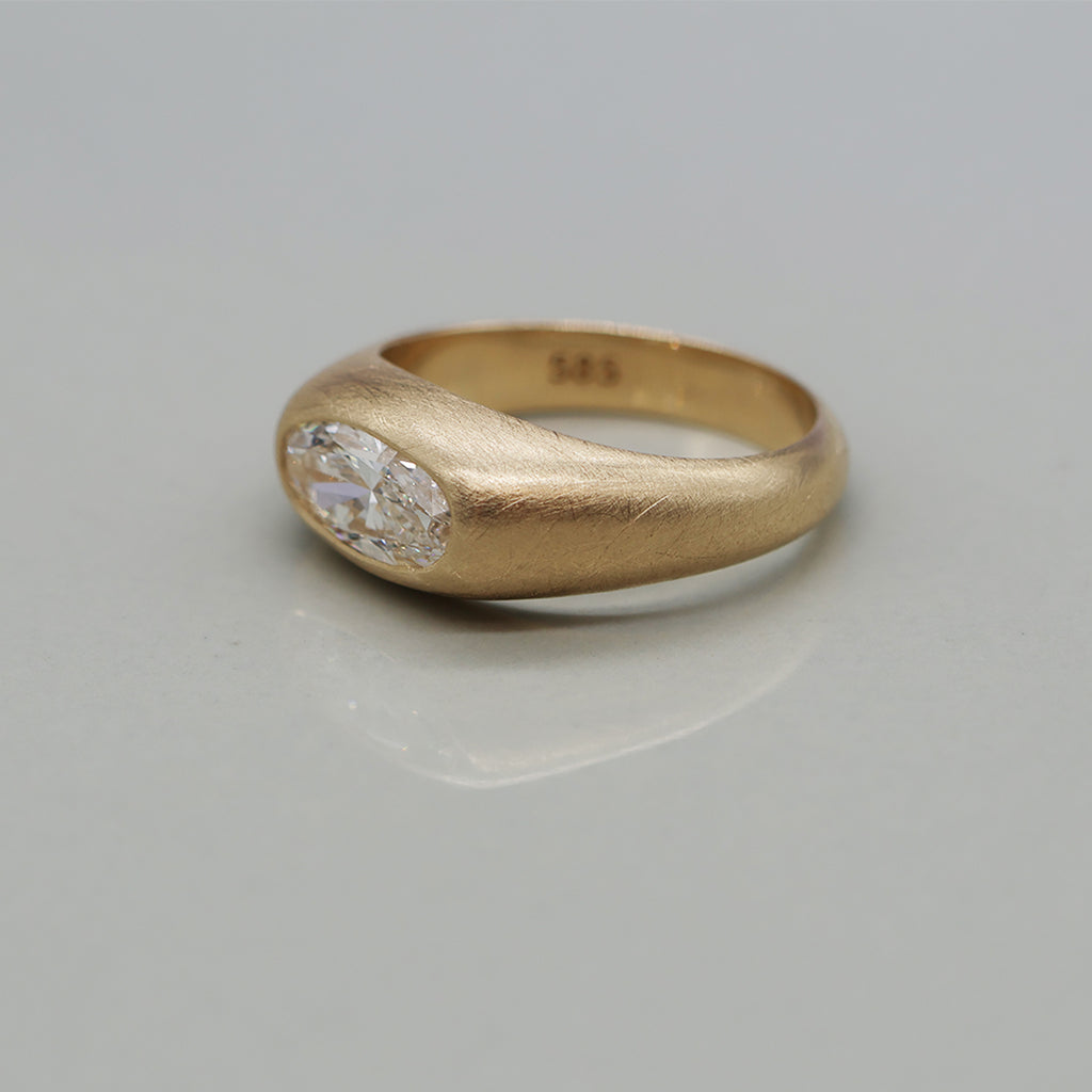 A yellow gold ring featuring a large oval brilliant-cut diamond centre stone with brushed texture, set against a clean white background with a soft reflection.