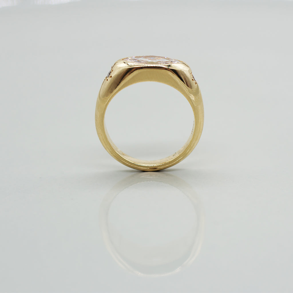 A yellow gold oval ring featuring a large marquis brilliant-cut diamond center stone and two small round diamond accents on the sides, set against a clean white background with a soft reflection.
