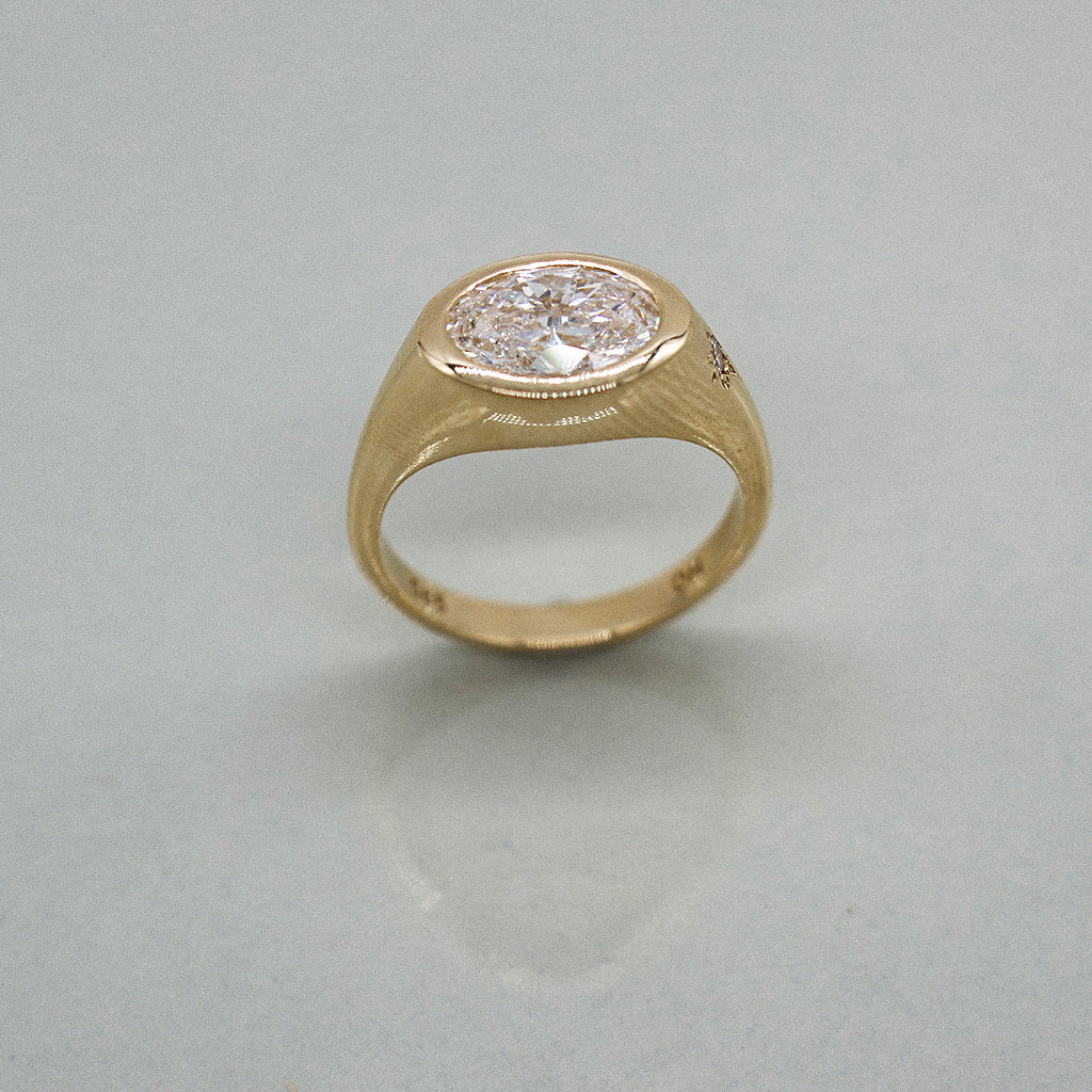 A yellow gold oval ring featuring a large oval brilliant-cut diamond centre stone set against a clean white background with a soft reflection.