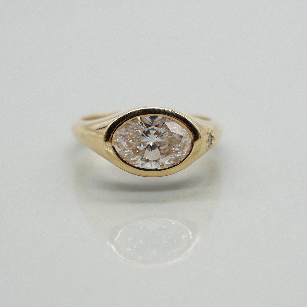 A yellow gold oval ring featuring a large oval brilliant-cut diamond centre stone set against a clean white background with a soft reflection.