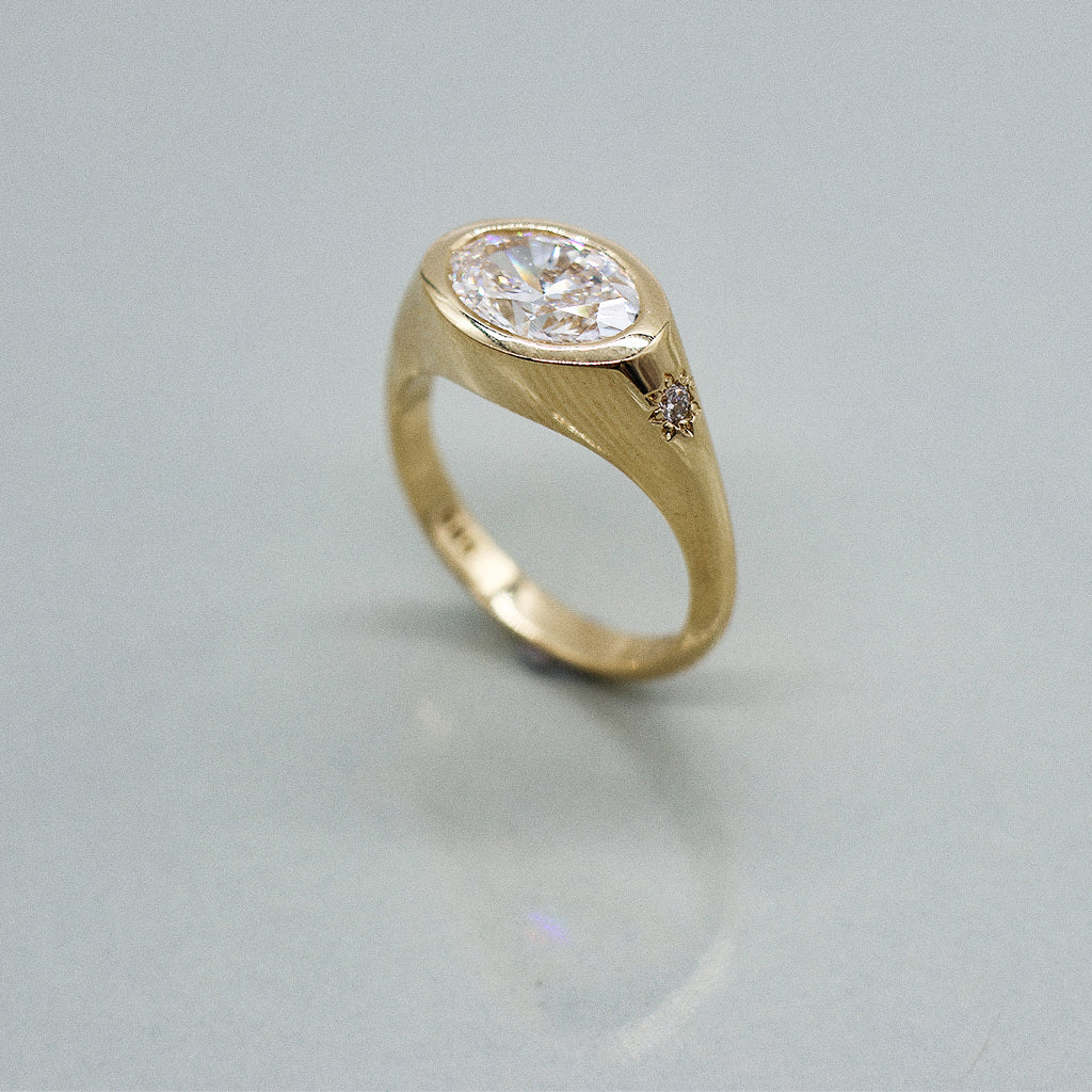 A yellow gold oval ring featuring a large oval brilliant-cut diamond centre stone set against a clean white background with a soft reflection.
