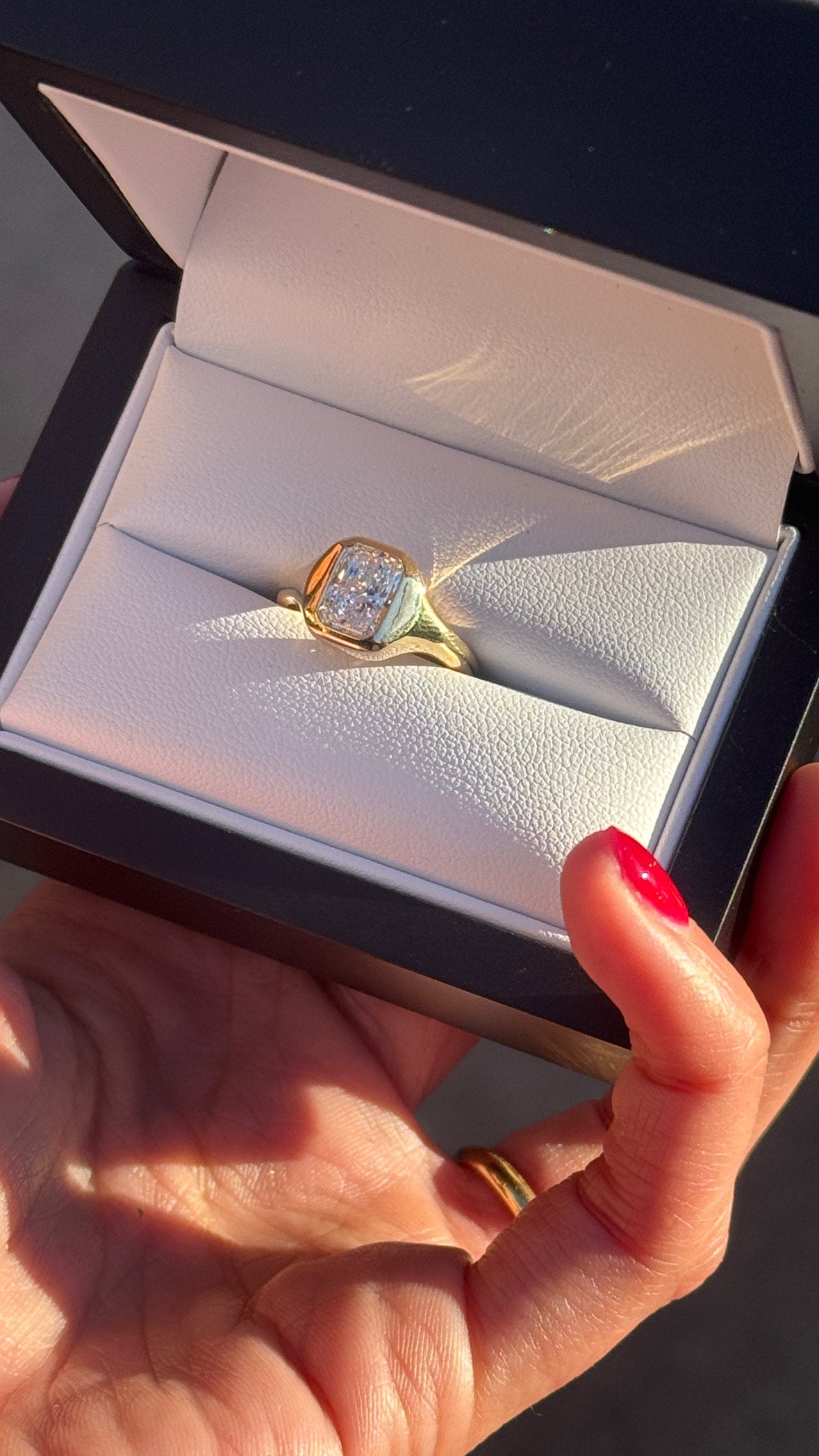 Gold ring with a diamond in an open jewelry box held by a hand.