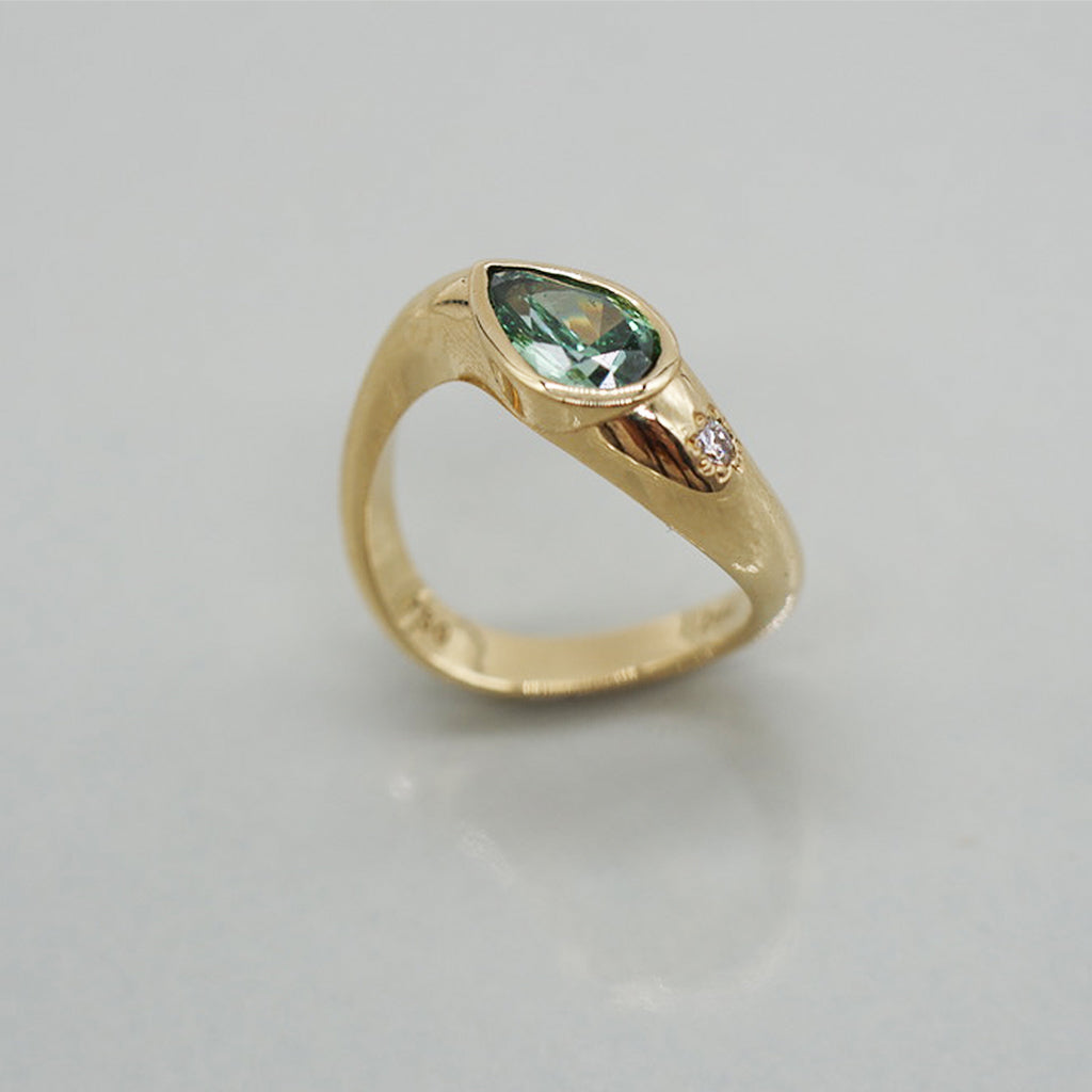 Gold ring with a green gemstone on a light gray background