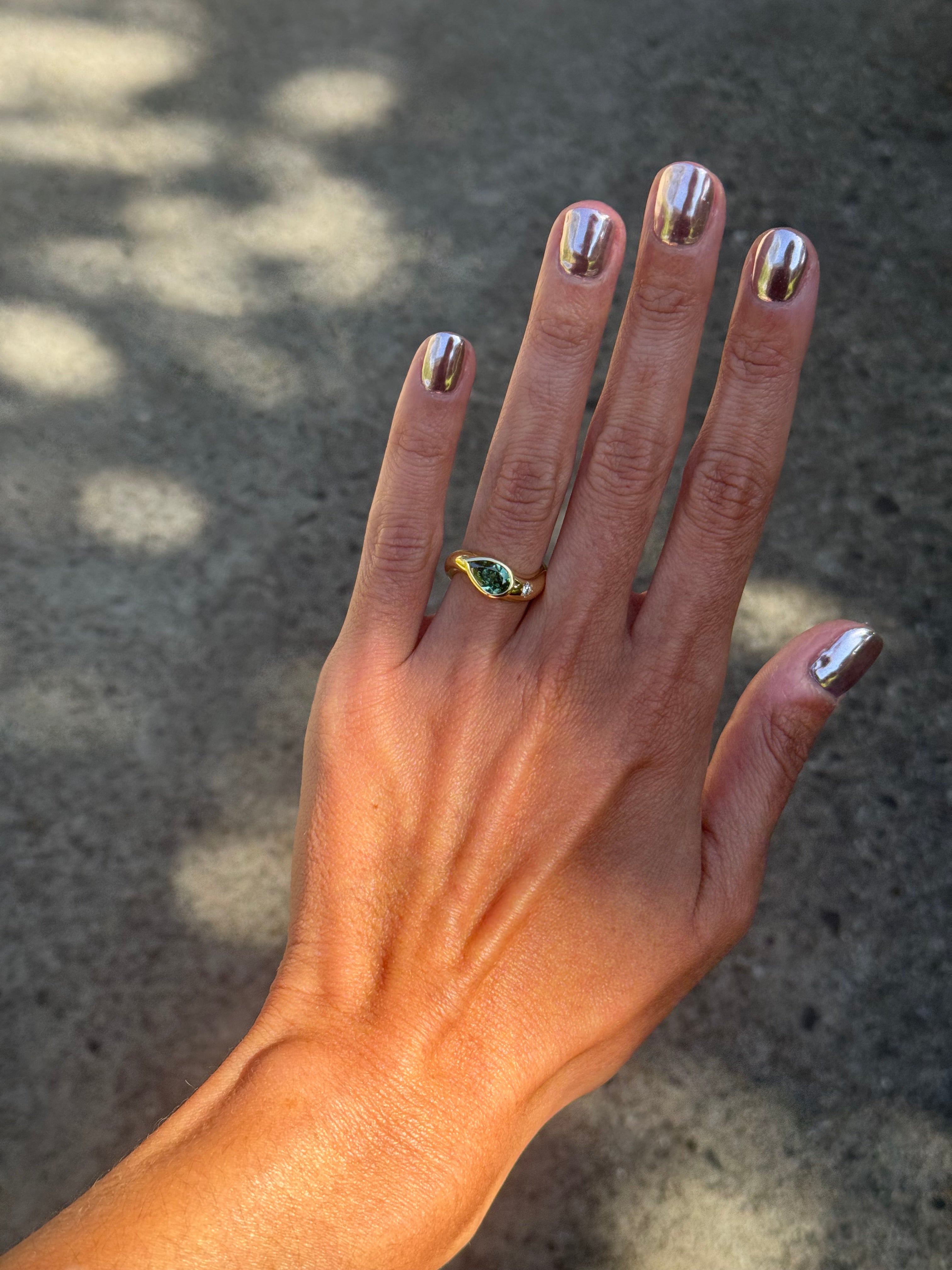 Hand with a gold ring featuring a green gemstone against a textured gray background