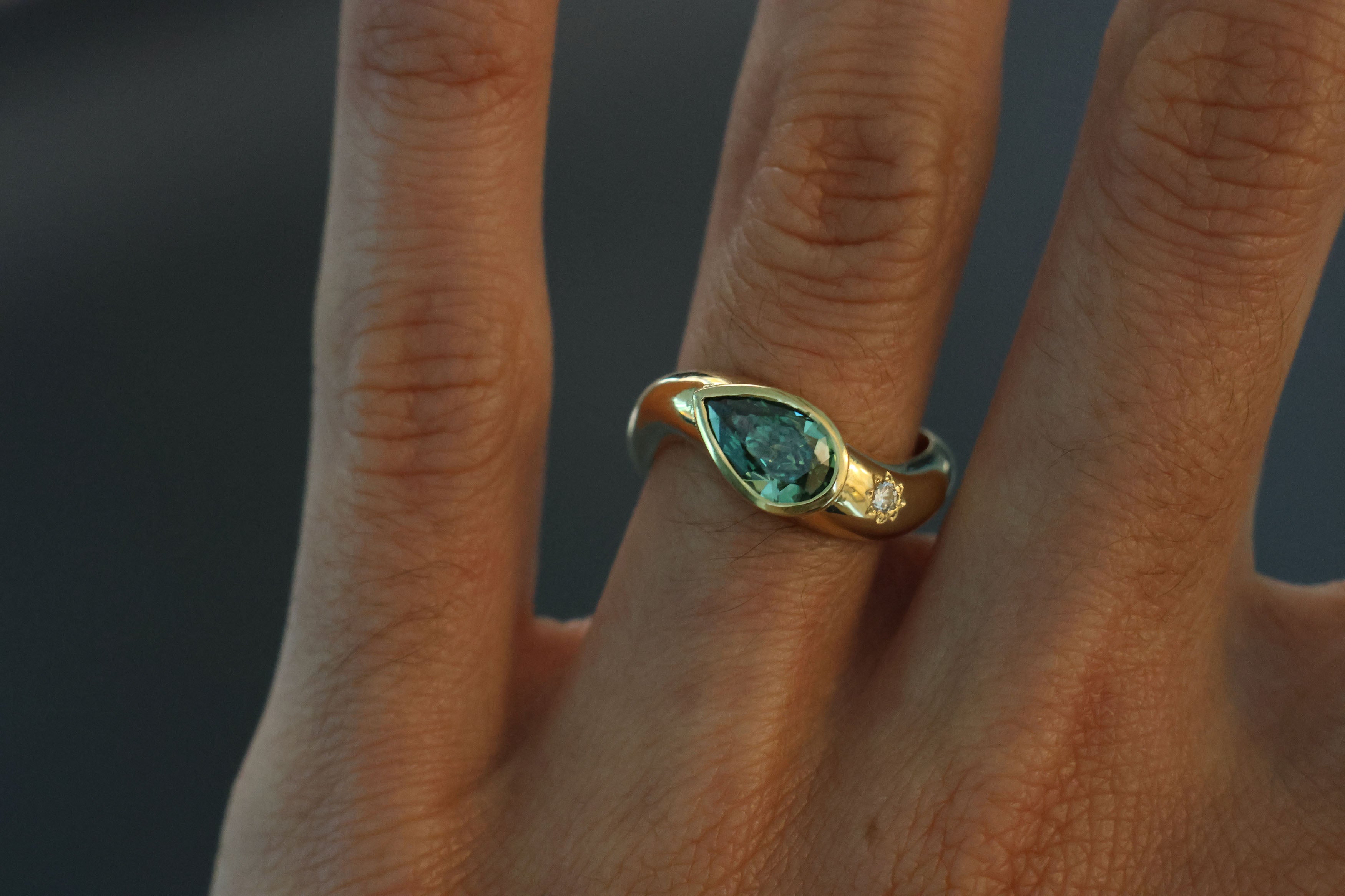 Gold ring with a green gemstone on a hand against a dark background