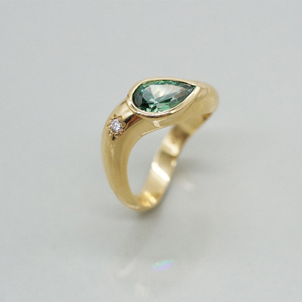 Gold ring with a green gemstone on a light gray background