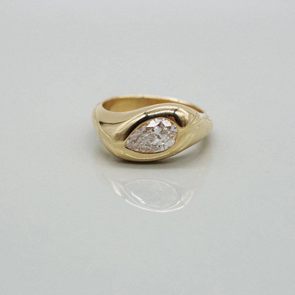 A yellow gold ring featuring a large pear cut diamond centre stone set against a clean white background with a soft reflection.