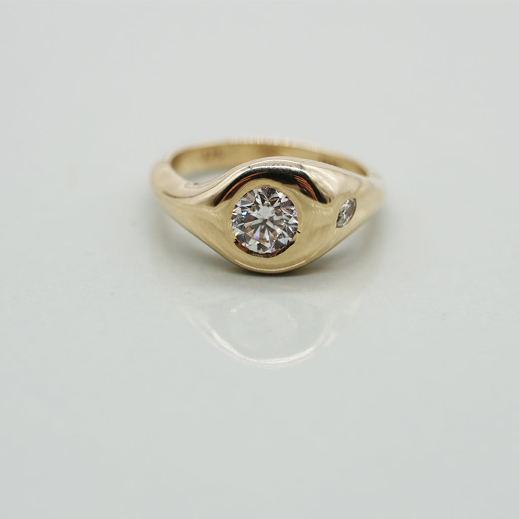 Gold ring with a round diamond and a small accent marquis diamond on a light gray background